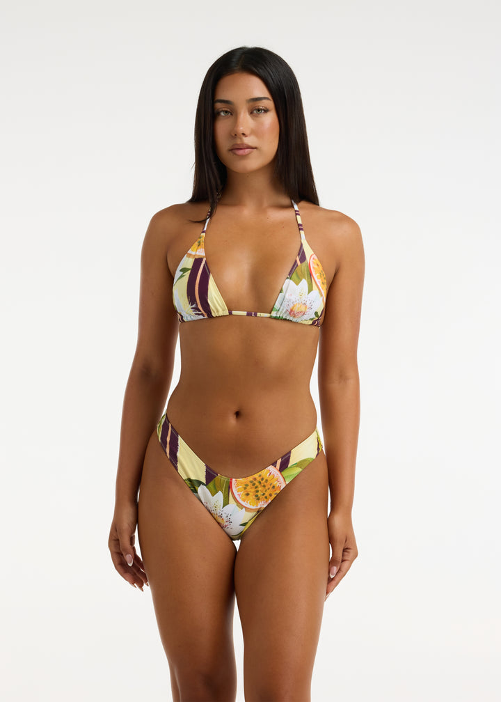 Model with long black hair wearing the Passiontini bikini top and Passiontini Midi Bottom in tropical passionfruit and floral print. The top features removable padding in a triangle halter shape and the bottoms are V shaped with a thick waistband. Bottoms sit high-waisted on the model.