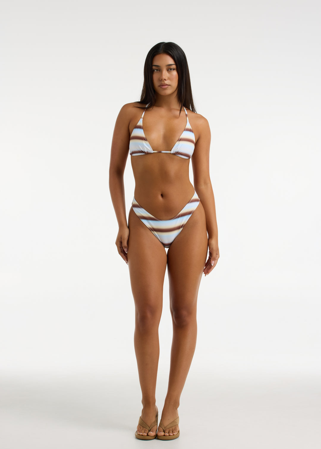 Model wearing Capri Swim Calypso Top and Calypso Midi Bottom bikini set. The print is blue and brown stripes. The top features removable padding in a triangle halter shape and the bottoms are V shaped with a thick waistband. Bottoms sit high-waisted on the model.